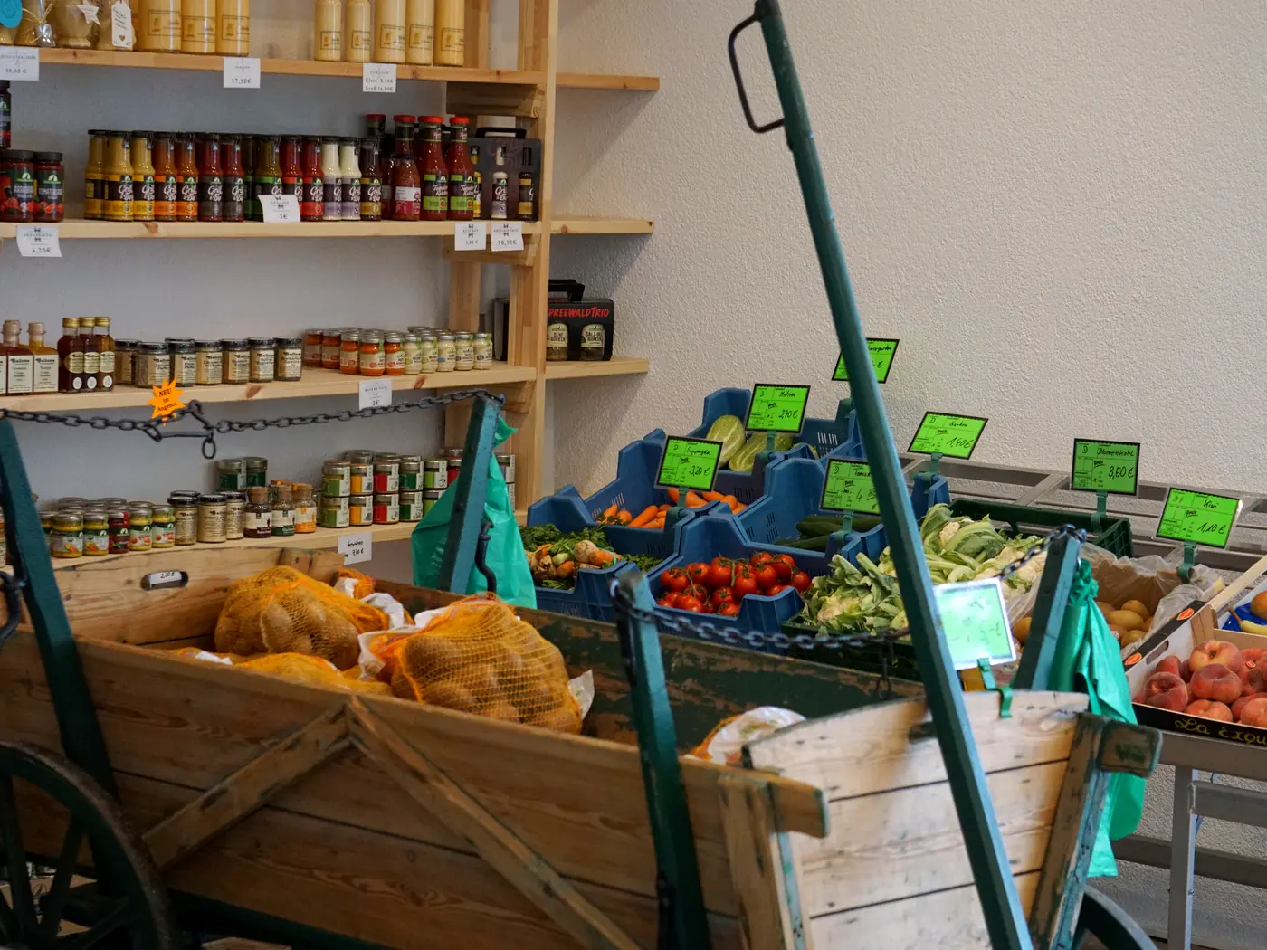 Kartoffeln in Netzen im hölzernen Handwagen des Hofladens, dahinter Regale mit Eingemachtem