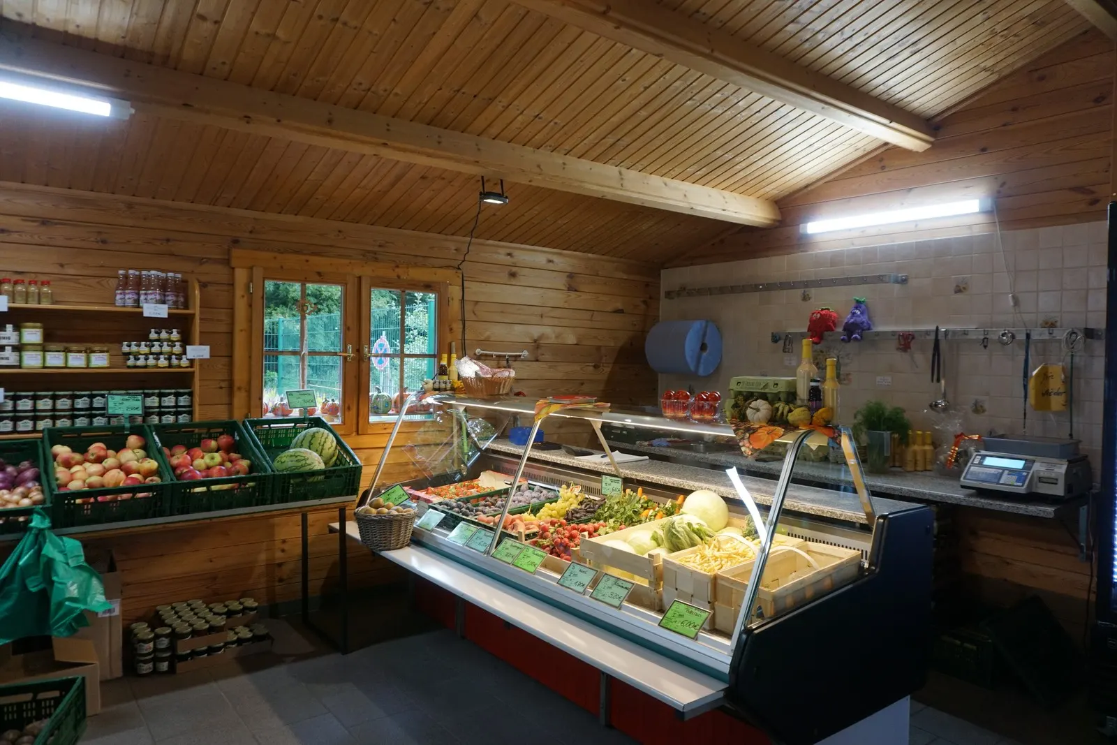 Blick in den Hofladen Lübben: Kühltheke mit Obst und Gemüse, Holzwände und Regale